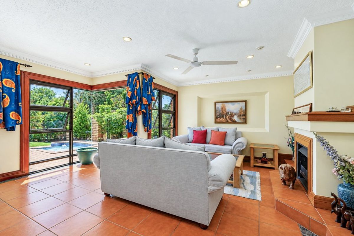 Spacious living room featuring a fireplace, tiled flooring, and large corner windows providing views of the outdoor pool area.