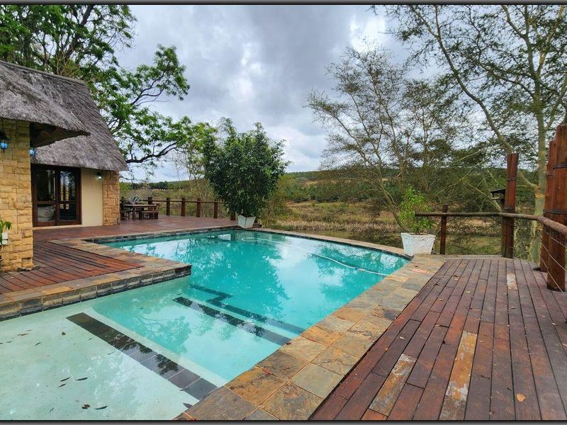 Outdoor pool area featuring timber decking, stone-clad building exterior with a thatched roof, and scenic landscape views.