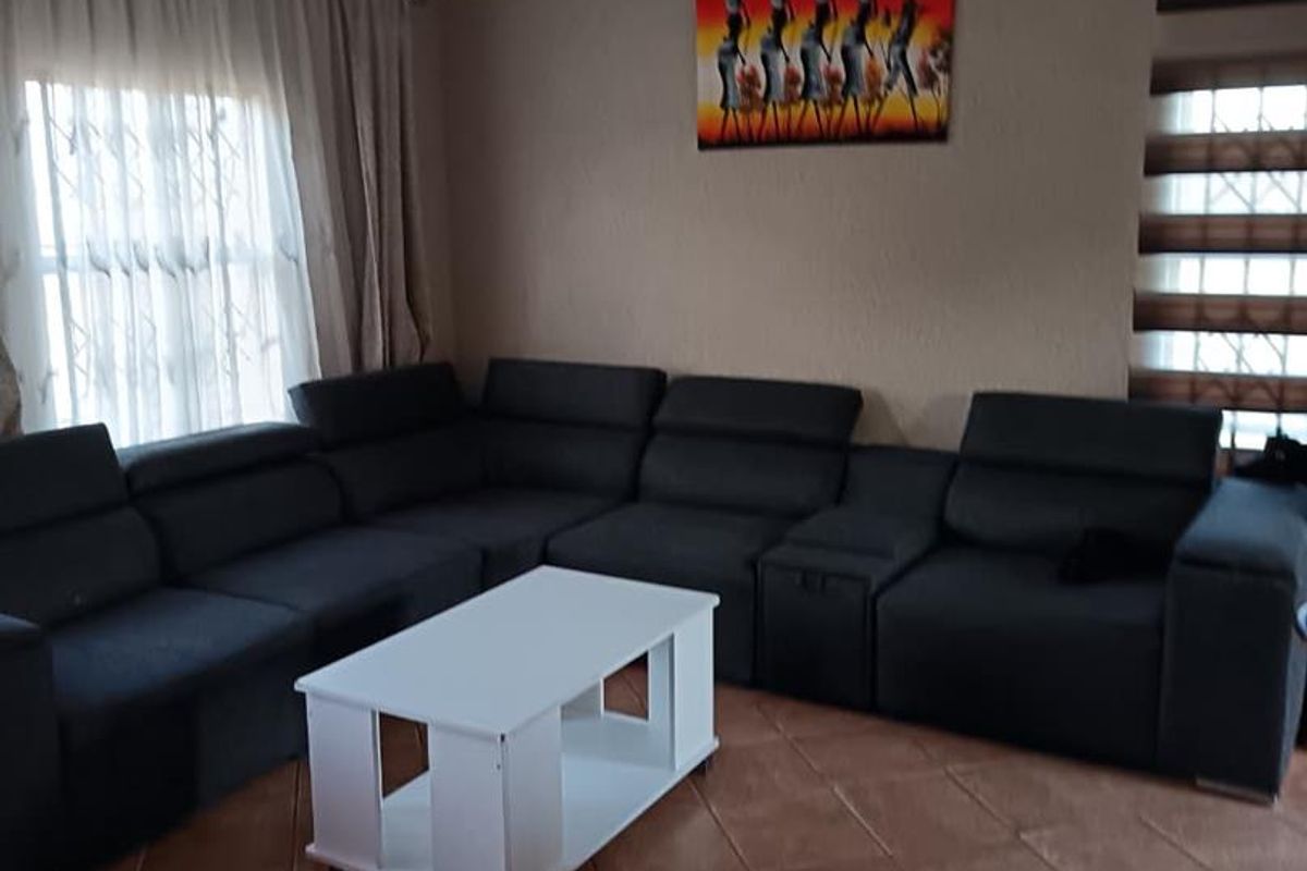 A comfortable living room featuring tiled flooring, neutral wall tones, and window treatments including curtains and roller blinds.