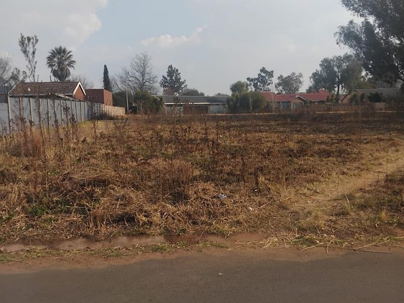 A vacant residential plot of land featuring perimeter fencing and direct access to an asphalt road, ready for development.