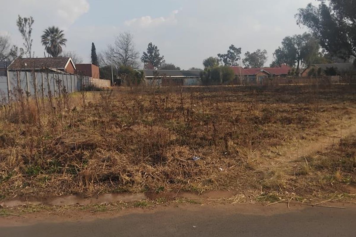 A vacant residential plot of land featuring perimeter fencing and direct access to an asphalt road, ready for development.