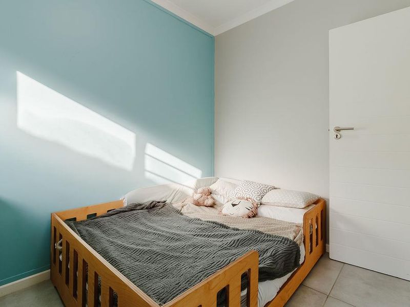 A bright and well-maintained bedroom featuring neutral tiled flooring, a modern internal door, and a vibrant blue accent wall.