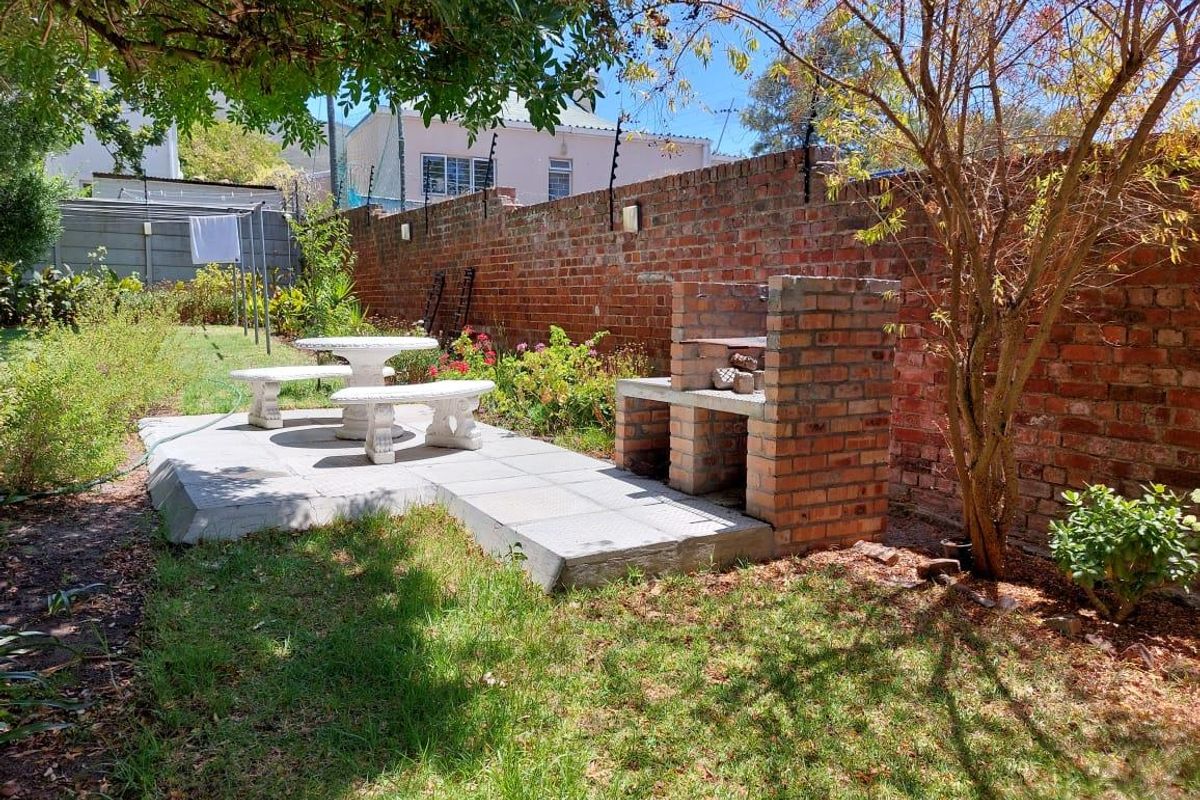 A private rear garden featuring a paved patio area, a built-in brick braai, and a secure brick boundary wall with electric fencing.