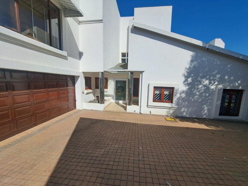 Front elevation of a modern house featuring a paved driveway, double garage, and a covered entrance with metal support columns.