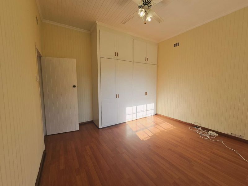 A bright, empty bedroom featuring timber panelled walls, laminate flooring, and ample built-in cupboard storage.
