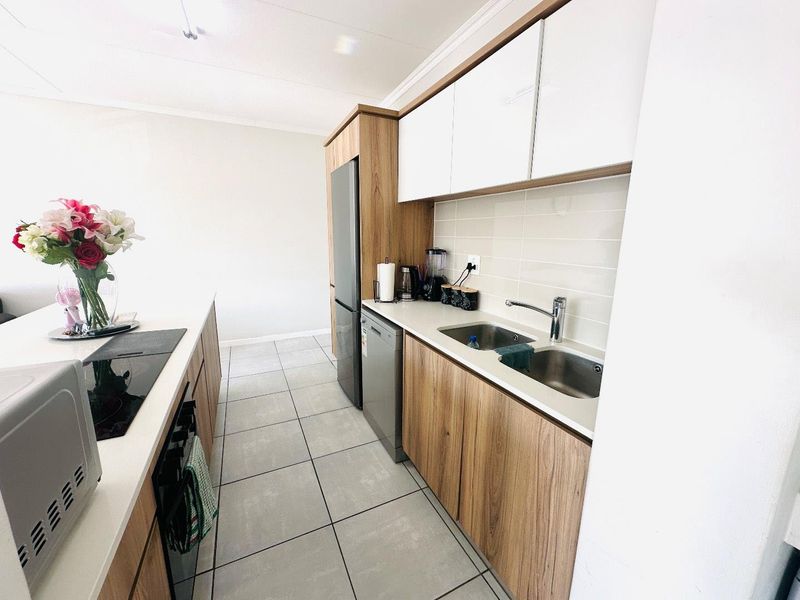 Modern kitchen featuring wood-grain cabinetry, white upper cabinets, stone countertops, a double basin sink, and a built-in ceramic hob with tiled flooring.