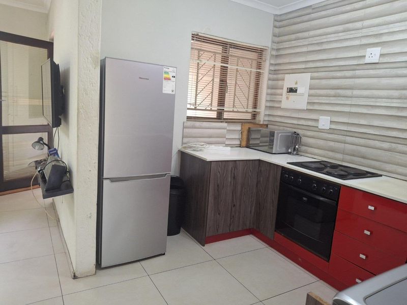 Compact kitchen featuring modern red and wood-grain cabinetry, tiled backsplash, built-in oven and hob, and neutral floor tiles.