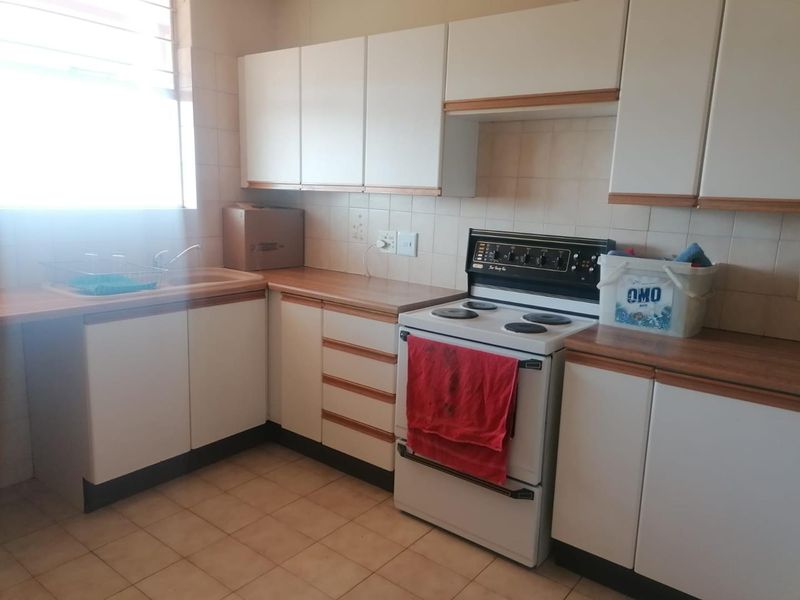 A functional kitchen featuring white cabinetry, laminate countertops, tiled backsplash, and a freestanding stove, offering a practical layout with potential for modern updates.