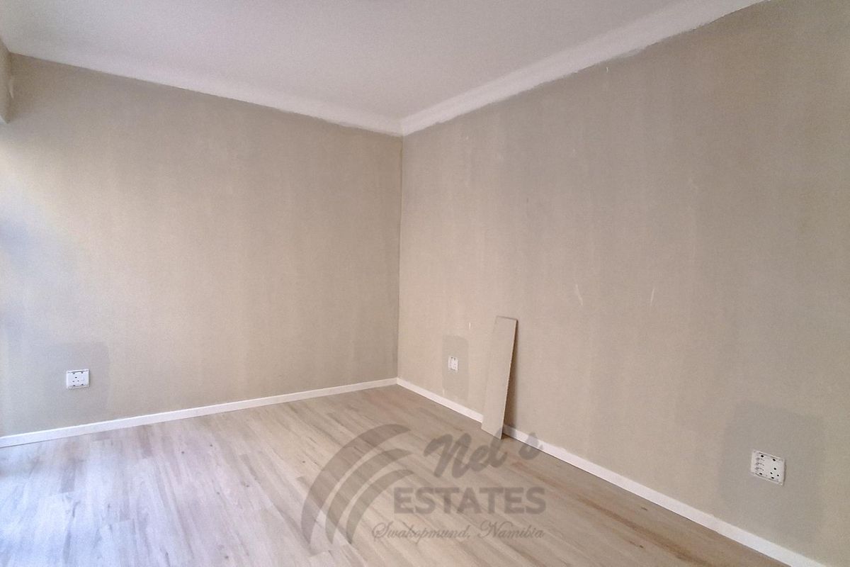 A bright, empty bedroom featuring neutral walls, modern laminate flooring, and a large sliding glass door providing natural light.