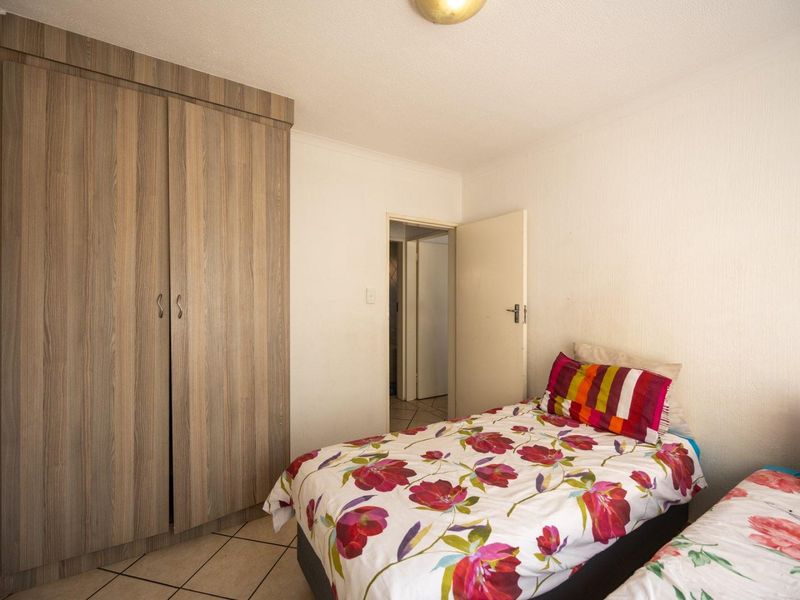 A bedroom featuring tiled flooring and a built-in wooden wardrobe, providing functional storage space within the apartment.
