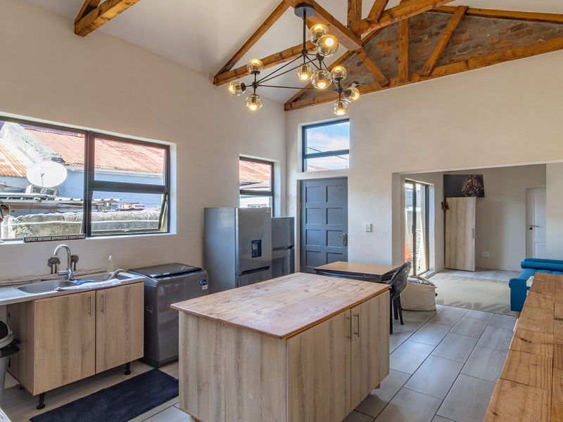 Spacious open-plan kitchen and living area featuring high vaulted ceilings with exposed timber trusses, modern cabinetry, and large windows providing ample natural light.