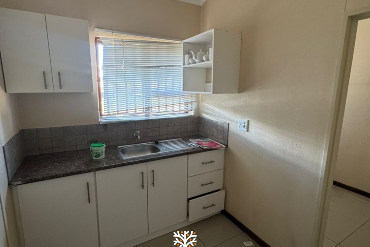 A compact kitchenette featuring white cabinetry, a granite-look countertop, a stainless steel sink, and tiled backsplash, suitable for office utility use.