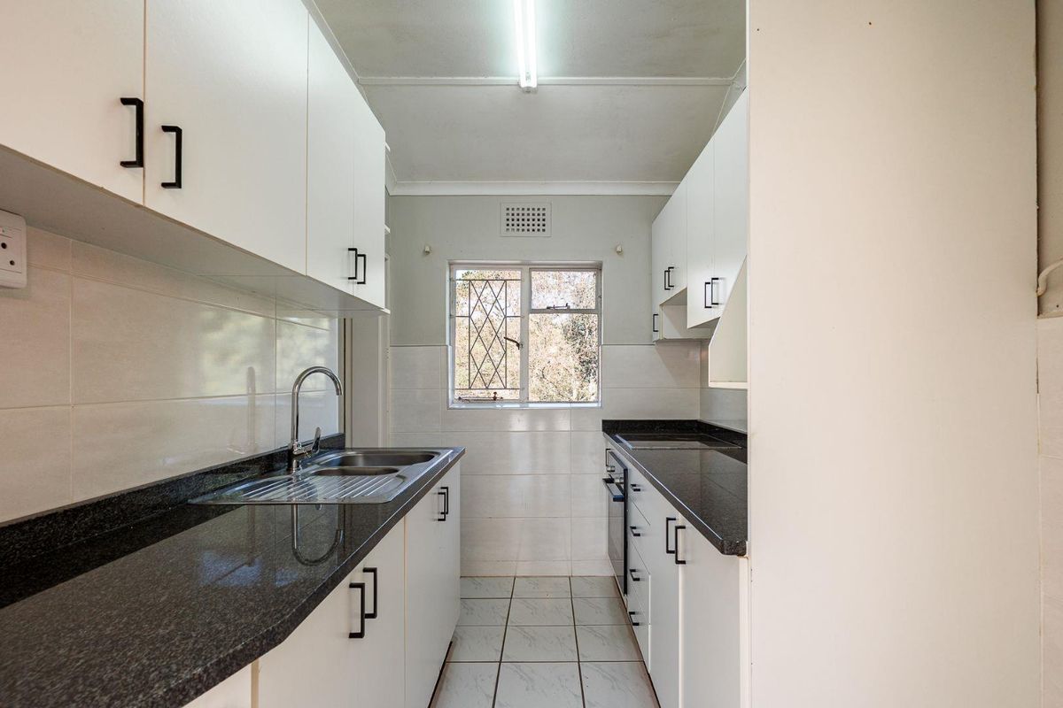 A functional galley-style kitchen featuring white cabinetry, dark granite countertops, stainless steel sink, and tiled finishes throughout.