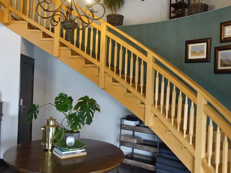 A spacious entrance hallway featuring a prominent wooden staircase with a classic balustrade and an elegant chandelier, set against a feature wall.