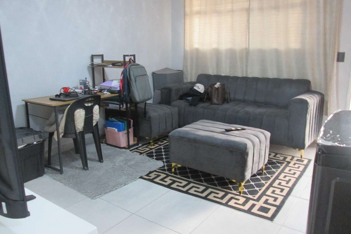 A functional living room area featuring tiled flooring and large windows with curtains, providing a neutral base for comfortable daily living.