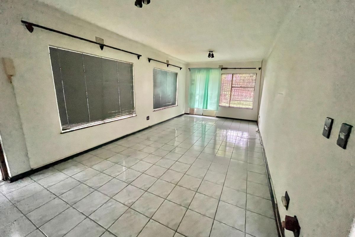 Spacious, empty living area featuring tiled flooring, security bars on windows, and venetian blinds, offering a blank canvas for renovation.