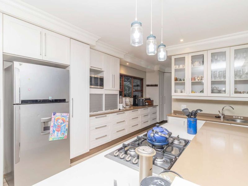 A well-appointed kitchen featuring white shaker-style cabinetry, stone countertops, a gas hob, and integrated appliances, complemented by elegant pendant lighting.