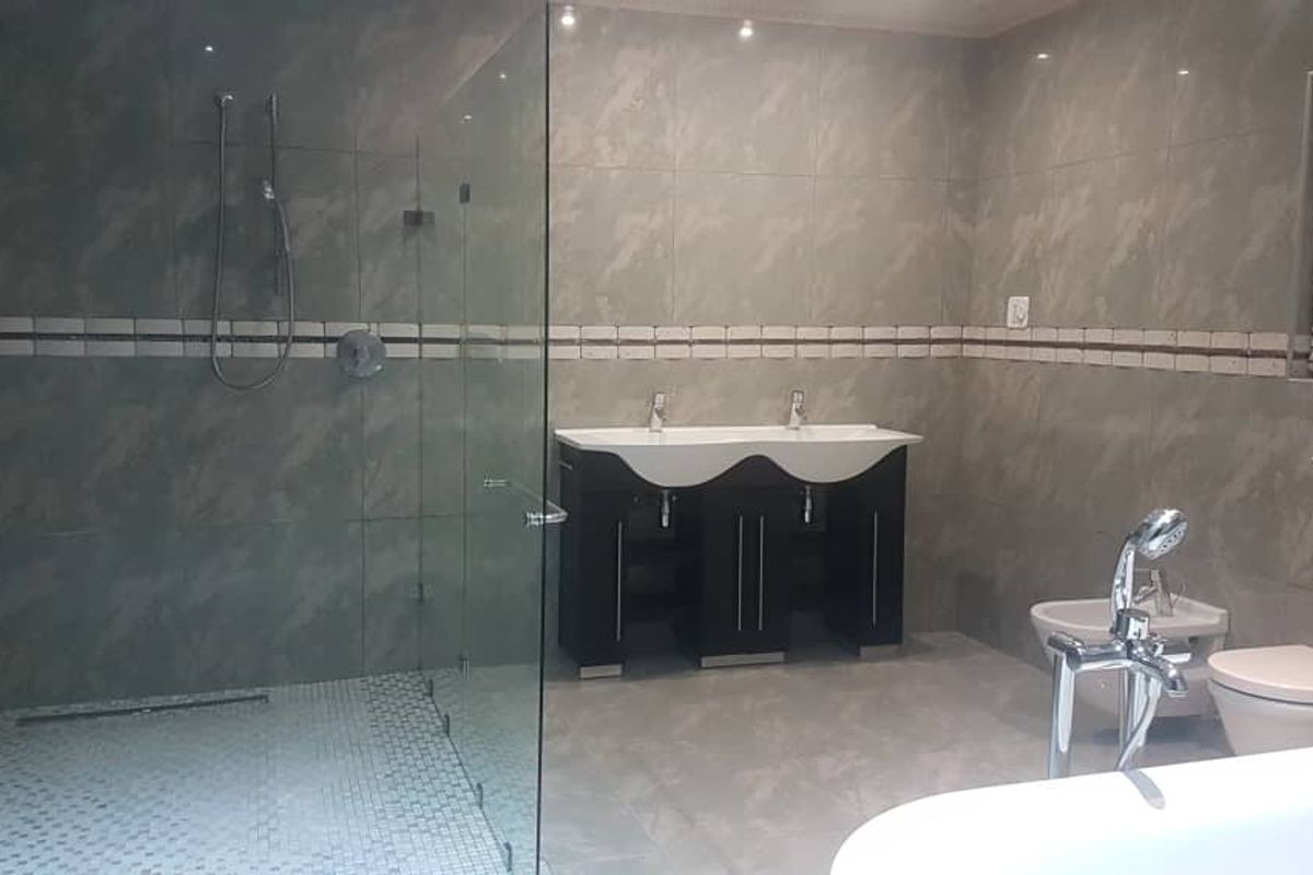 Modern bathroom featuring a large walk-in glass shower, double vanity with integrated sinks, a freestanding bathtub, and a bidet.