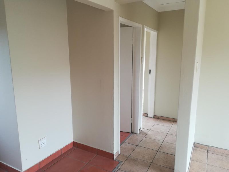 A vacant hallway featuring tiled flooring and access to multiple internal rooms, showing signs of wear and tear on the finishes.