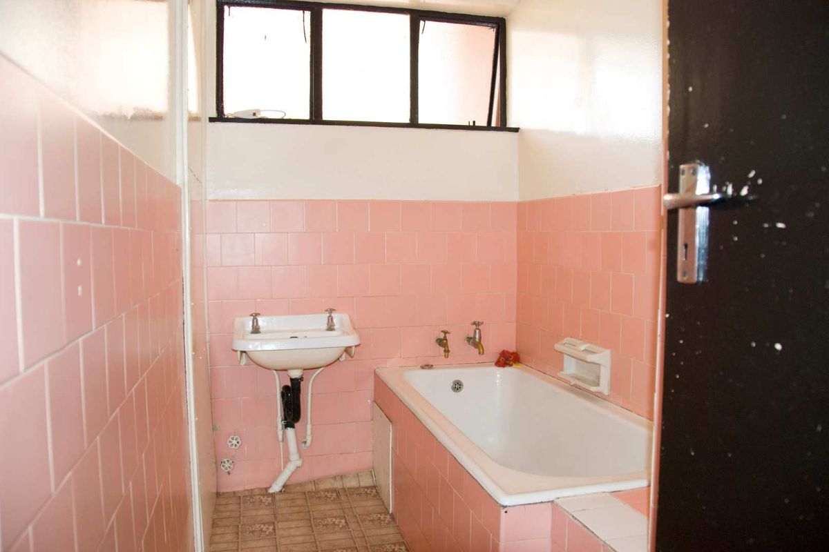 A dated bathroom featuring pink wall tiles, a built-in bathtub, and a wall-mounted basin with a high-level window.