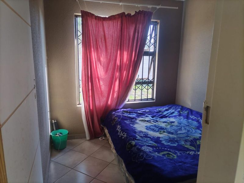 A compact bedroom featuring tiled flooring, a built-in cupboard, and a window fitted with a security gate.
