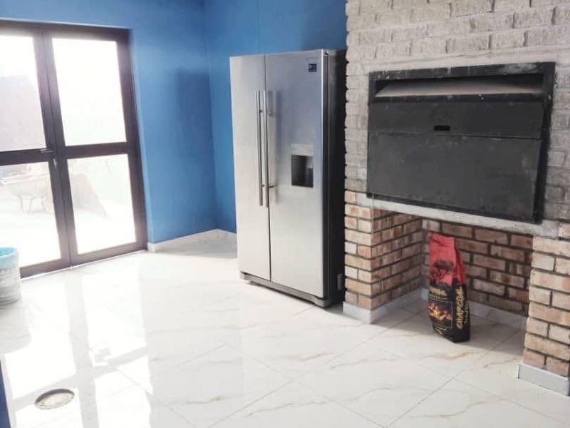 An indoor entertainment area featuring a built-in brick braai, polished marble-look tiled flooring, and direct access to the outdoors via sliding glass doors.