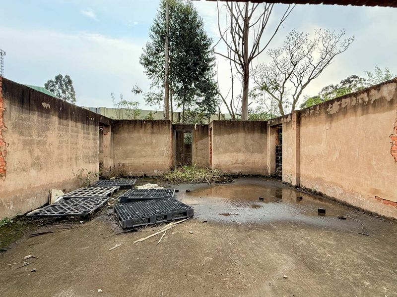 An open-air utility space featuring concrete masonry walls and a concrete slab floor, currently in a state of significant disrepair.