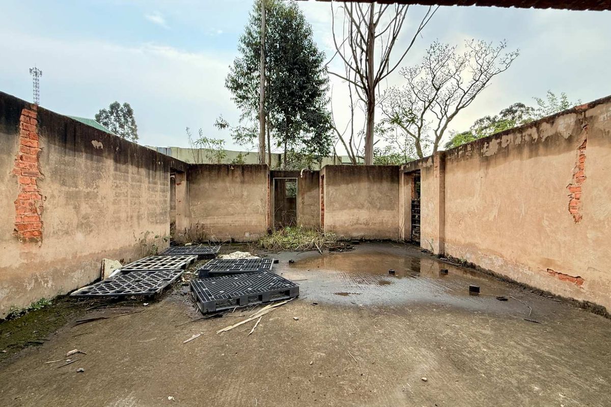 An open-air utility space featuring concrete masonry walls and a concrete slab floor, currently in a state of significant disrepair.