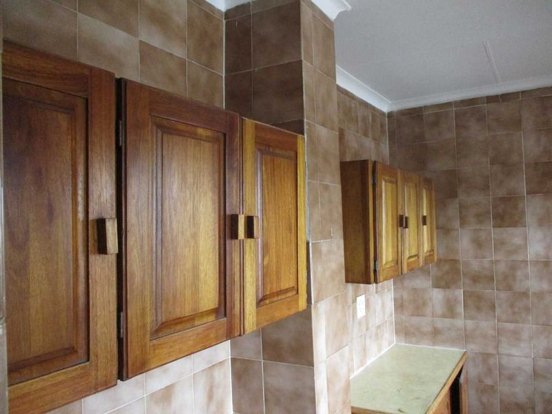 A dated kitchen area featuring traditional wooden cabinetry and full-height tiled walls, offering a blank canvas for modern renovation.