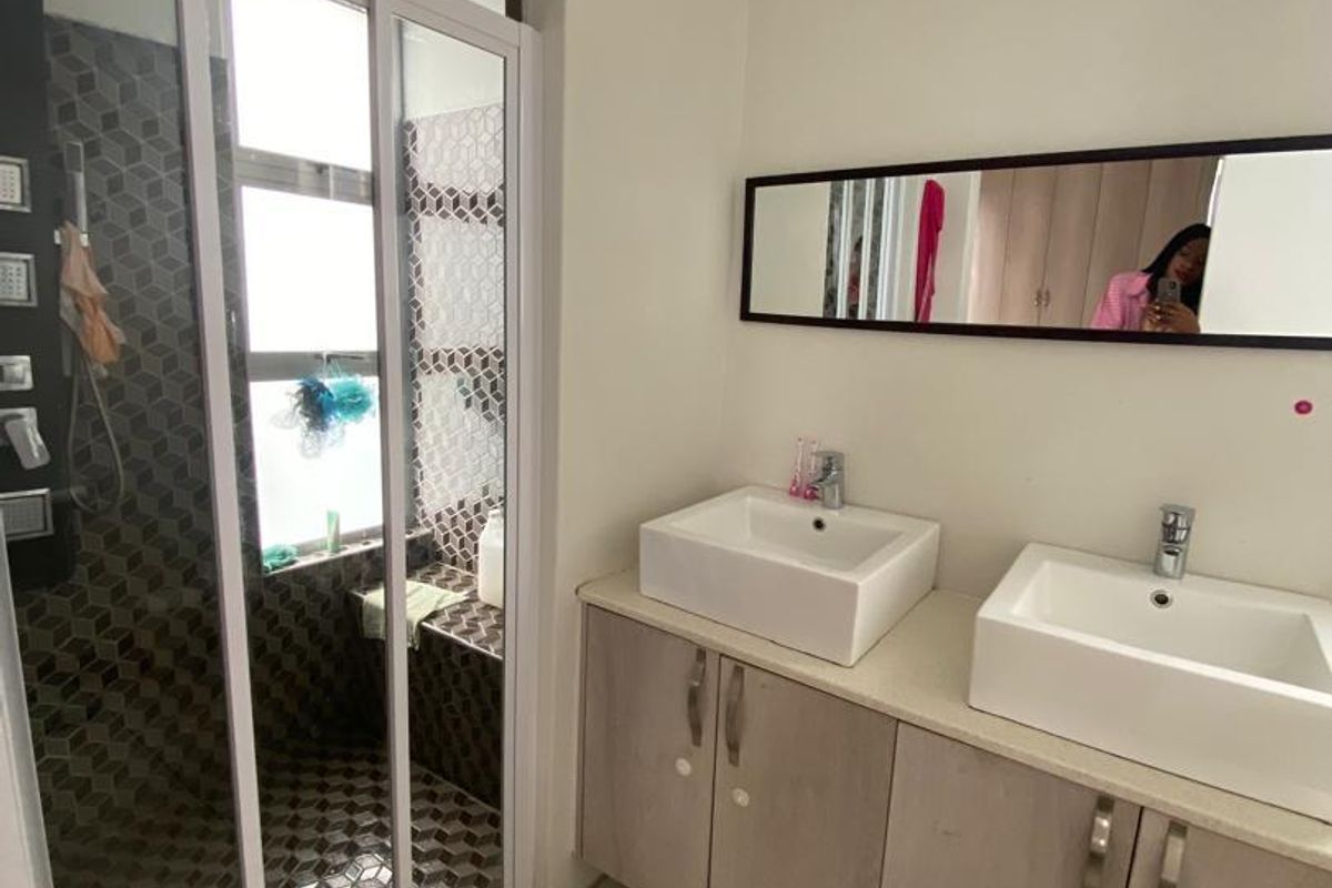 Modern bathroom featuring a double vanity with vessel sinks, a glass-enclosed shower with patterned tiling, and a wall-mounted mirror.