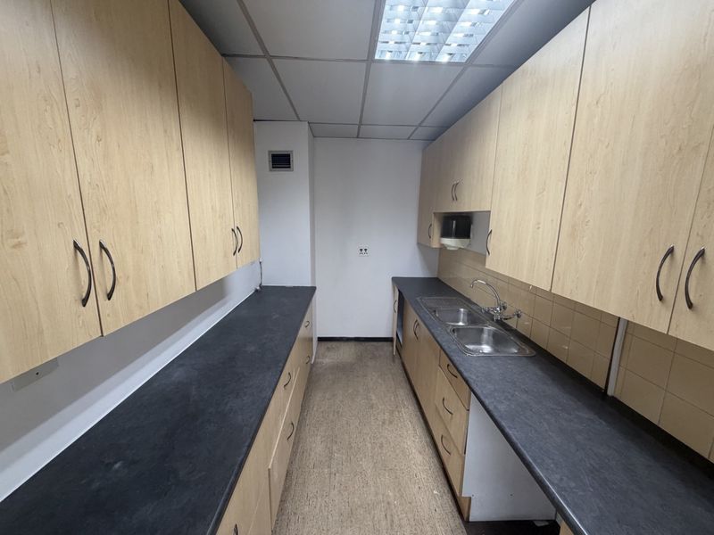 A functional industrial kitchenette featuring ample laminate cabinetry, dark countertops, a double stainless steel sink, and practical tiled splashbacks.