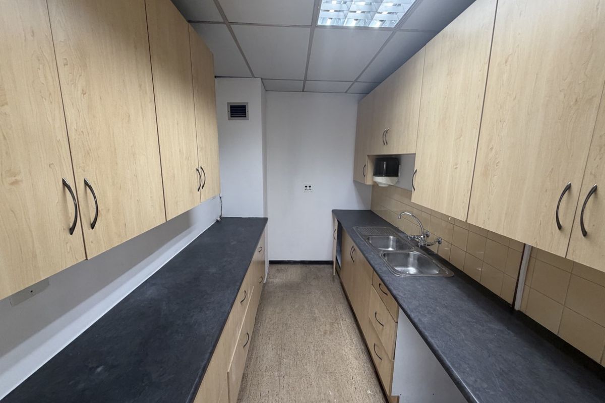A functional industrial kitchenette featuring ample laminate cabinetry, dark countertops, a double stainless steel sink, and practical tiled splashbacks.