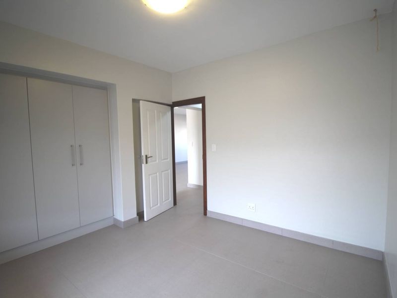 A clean, empty bedroom featuring neutral tiled flooring, built-in cupboards, and a simple interior door leading to an adjacent space.