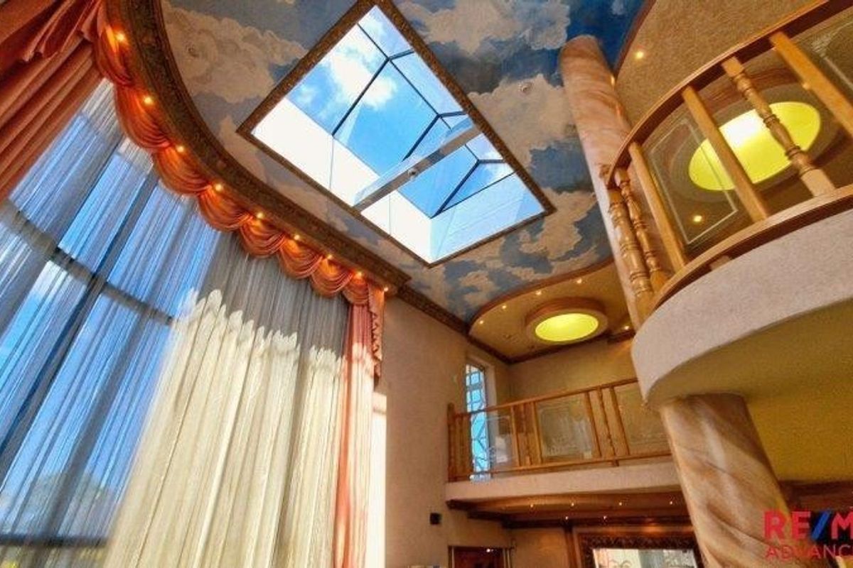 Spacious double-volume living area featuring a large skylight, decorative cloud-painted ceiling, and an elevated mezzanine level with wooden balustrades.