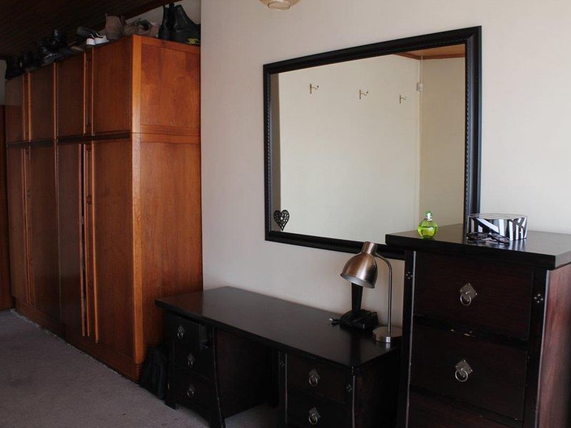 A bedroom featuring a large built-in wooden wardrobe and carpeted flooring, providing ample storage space.