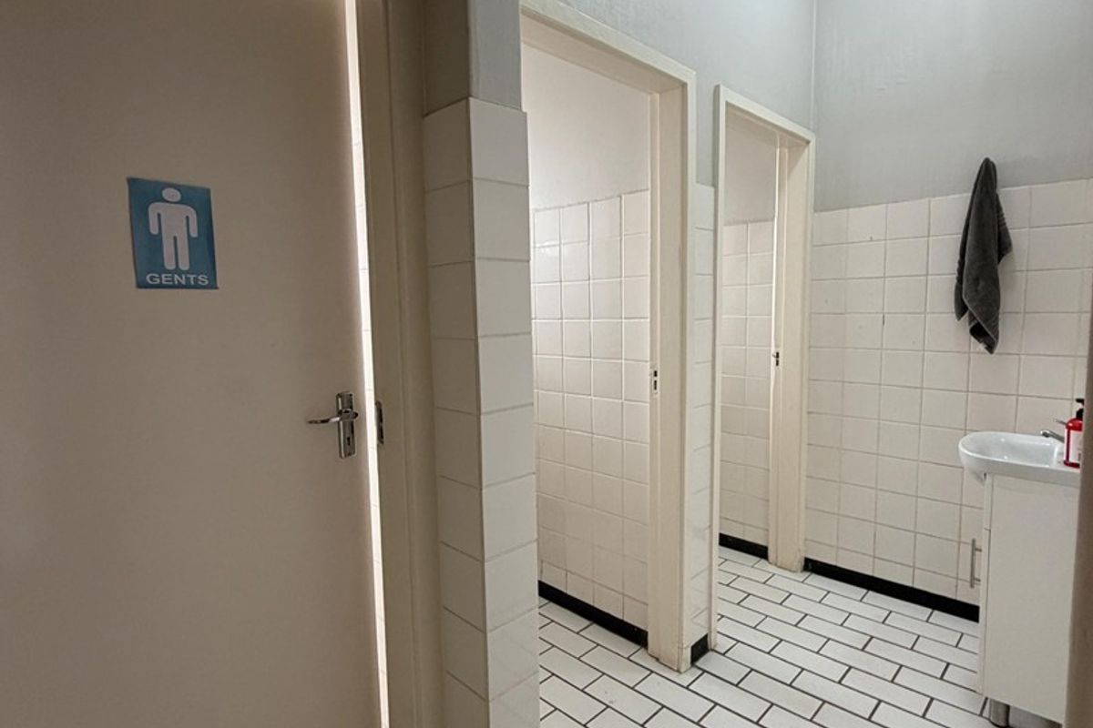 A functional gents restroom featuring tiled flooring, wall tiling, and a pedestal basin with multiple stall access points.
