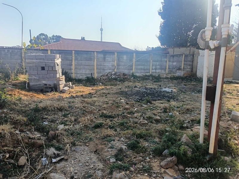 A view of a vacant residential plot featuring a precast concrete boundary wall and existing plumbing infrastructure.