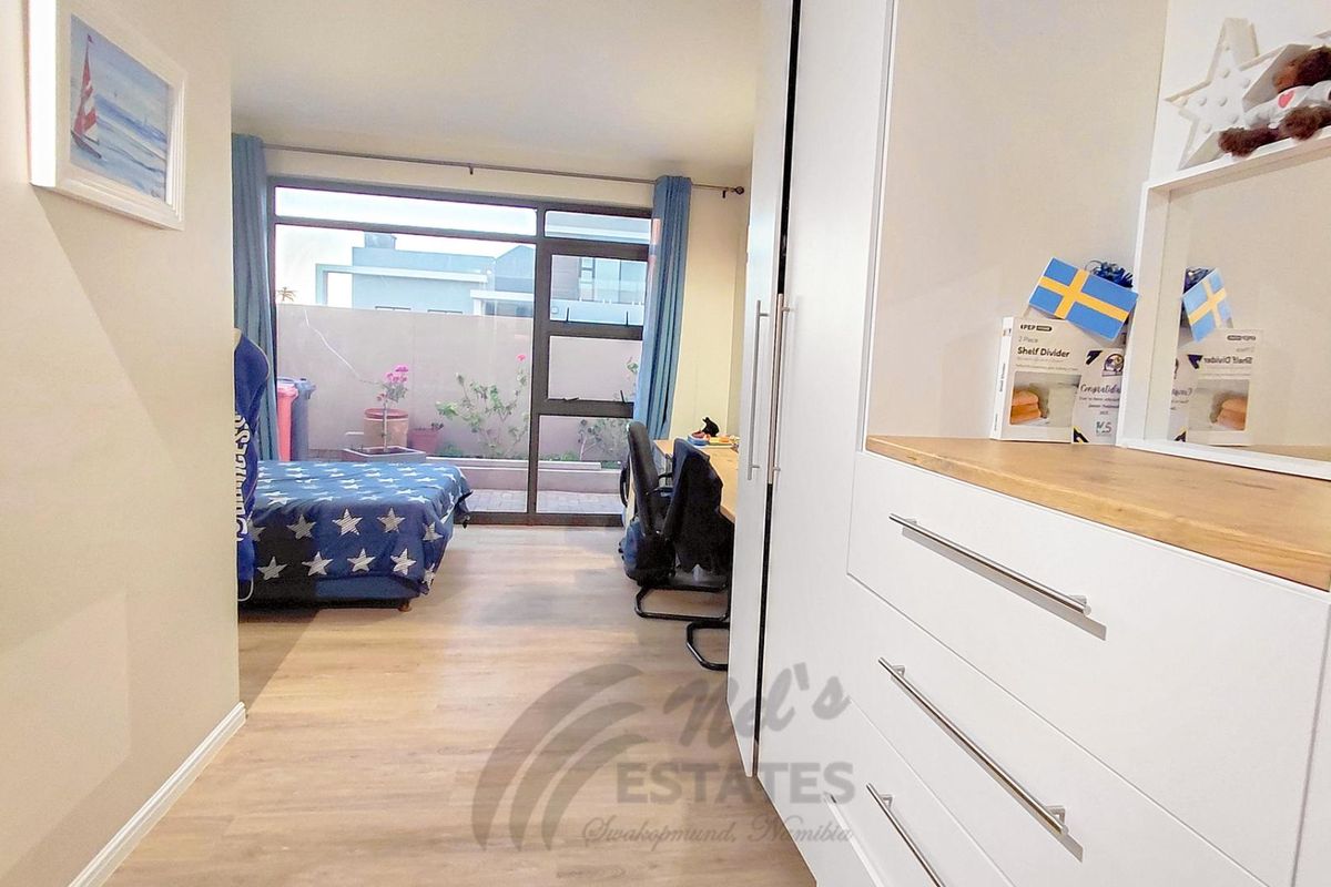 A bright bedroom featuring built-in cabinetry, light wood-look flooring, and large sliding glass doors providing access to a private outdoor patio area.