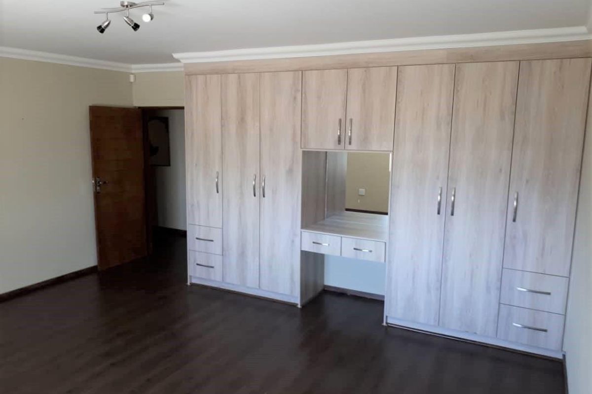 A spacious bedroom featuring extensive built-in wooden cabinetry with an integrated vanity area, dark laminate flooring, and modern ceiling-mounted spotlight fixtures.