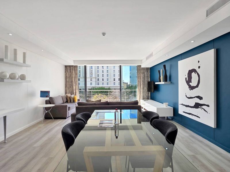 A bright and modern open-plan living and dining area featuring light wood-look flooring, a bold blue feature wall, and large sliding doors to the balcony.