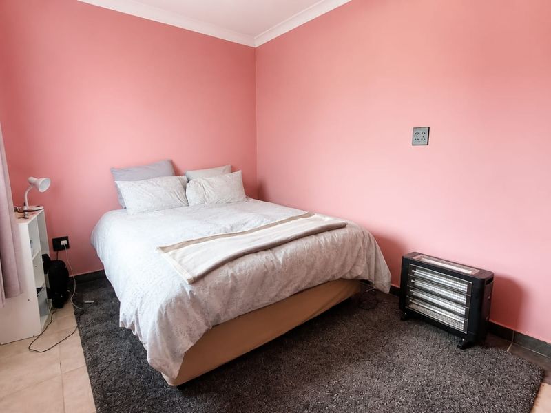 A bedroom featuring pink painted walls, tiled flooring, and a standard door, providing a functional and simple living space.