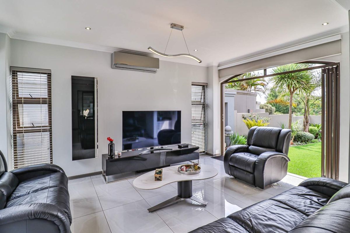 Modern living room featuring large format floor tiles, recessed downlighting, a wall-mounted air conditioning unit, and large folding doors opening to a landscaped garden.