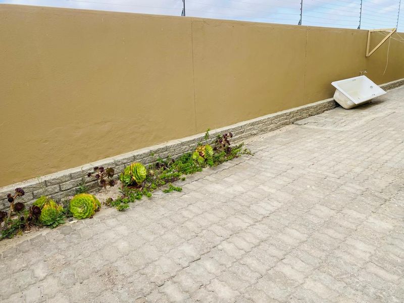 A paved outdoor area featuring a boundary wall with installed electric fencing and a small landscaped garden bed.