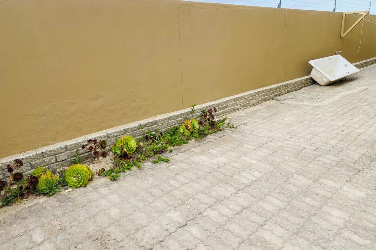 A paved outdoor area featuring a boundary wall with installed electric fencing and a small landscaped garden bed.