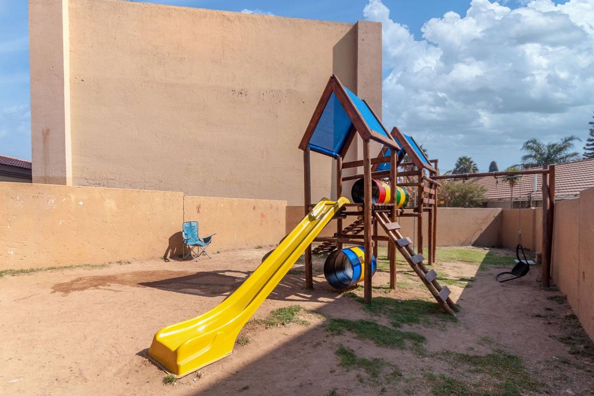 A private outdoor courtyard area featuring a wooden jungle gym with a slide, enclosed by high boundary walls.