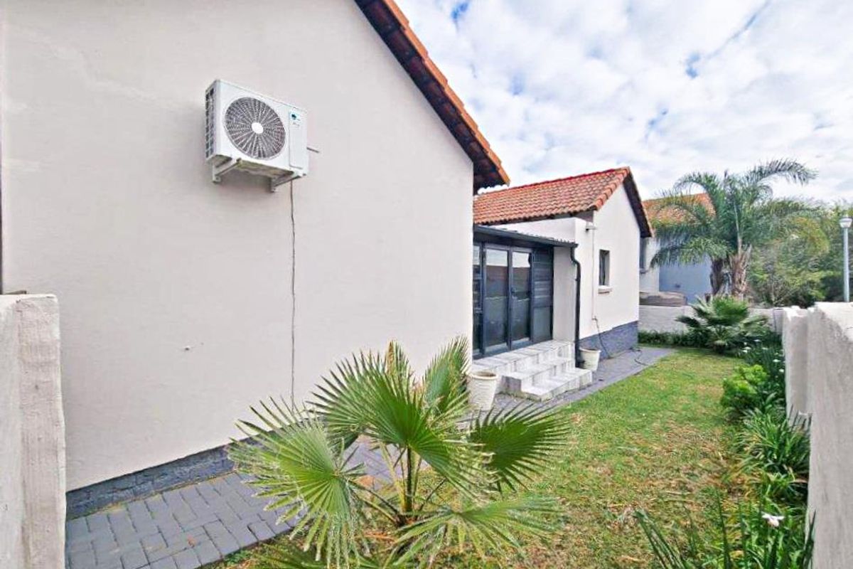 A view of the rear exterior of the house featuring a small garden, paved walkway, and an external air conditioning unit.