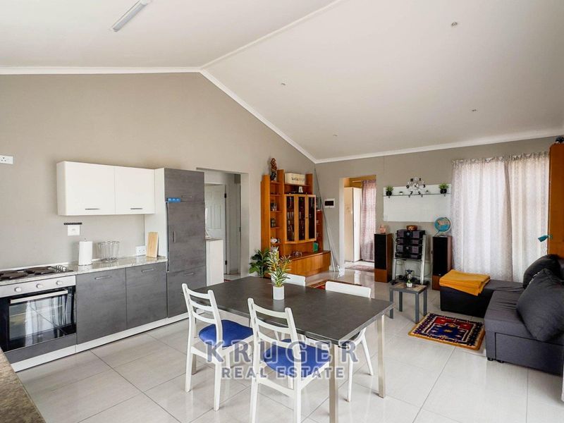 Open-plan living area featuring a modern kitchen with built-in cabinetry, oven, hob, and tiled flooring under a vaulted ceiling.