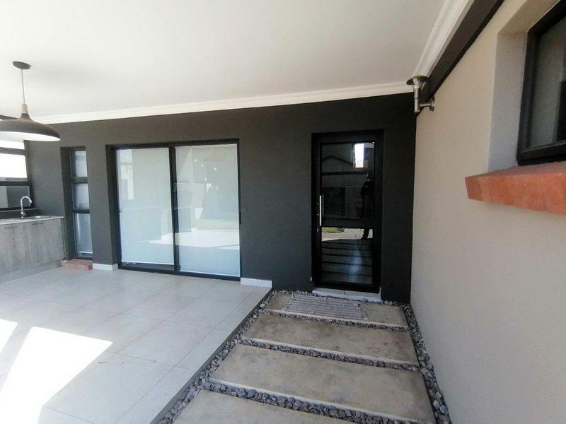 A modern covered patio featuring tiled flooring, built-in cabinetry with a sink, and direct access to the interior through sliding and glass doors.