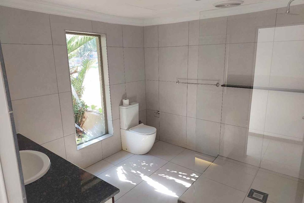 Modern bathroom featuring large format wall and floor tiles, a frameless glass walk-in shower, and a granite-topped vanity.