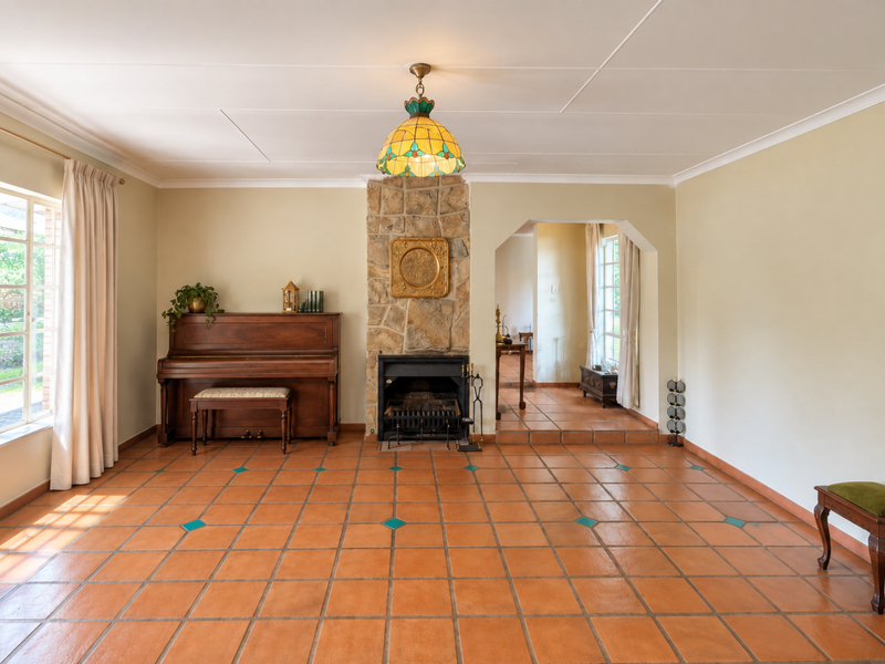 Spacious living room featuring terracotta tile flooring, a central stone fireplace, and a decorative pendant light, leading into an adjacent room through an archway.